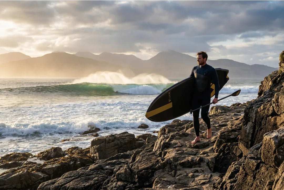 Performance SUP paddler in full wetsuit carrying Loco hard board over tropical rocky reef after surf session