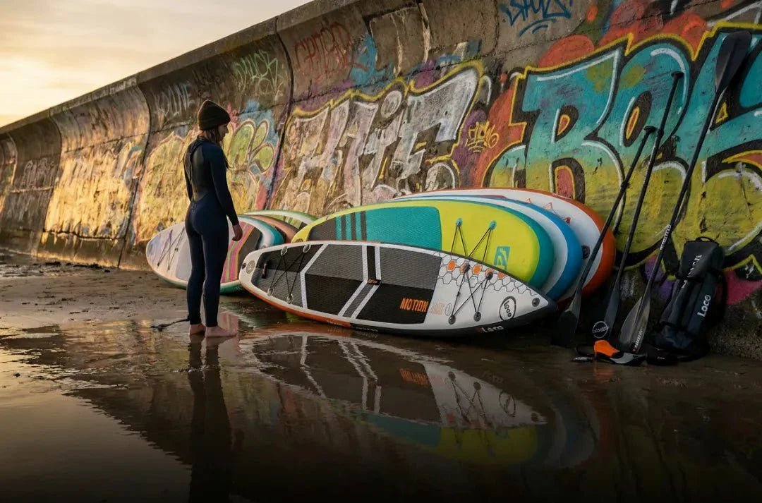 Woman reviewing Loco Motion Air and multiple inflatable SUP boards against colourful graffiti wall in UK