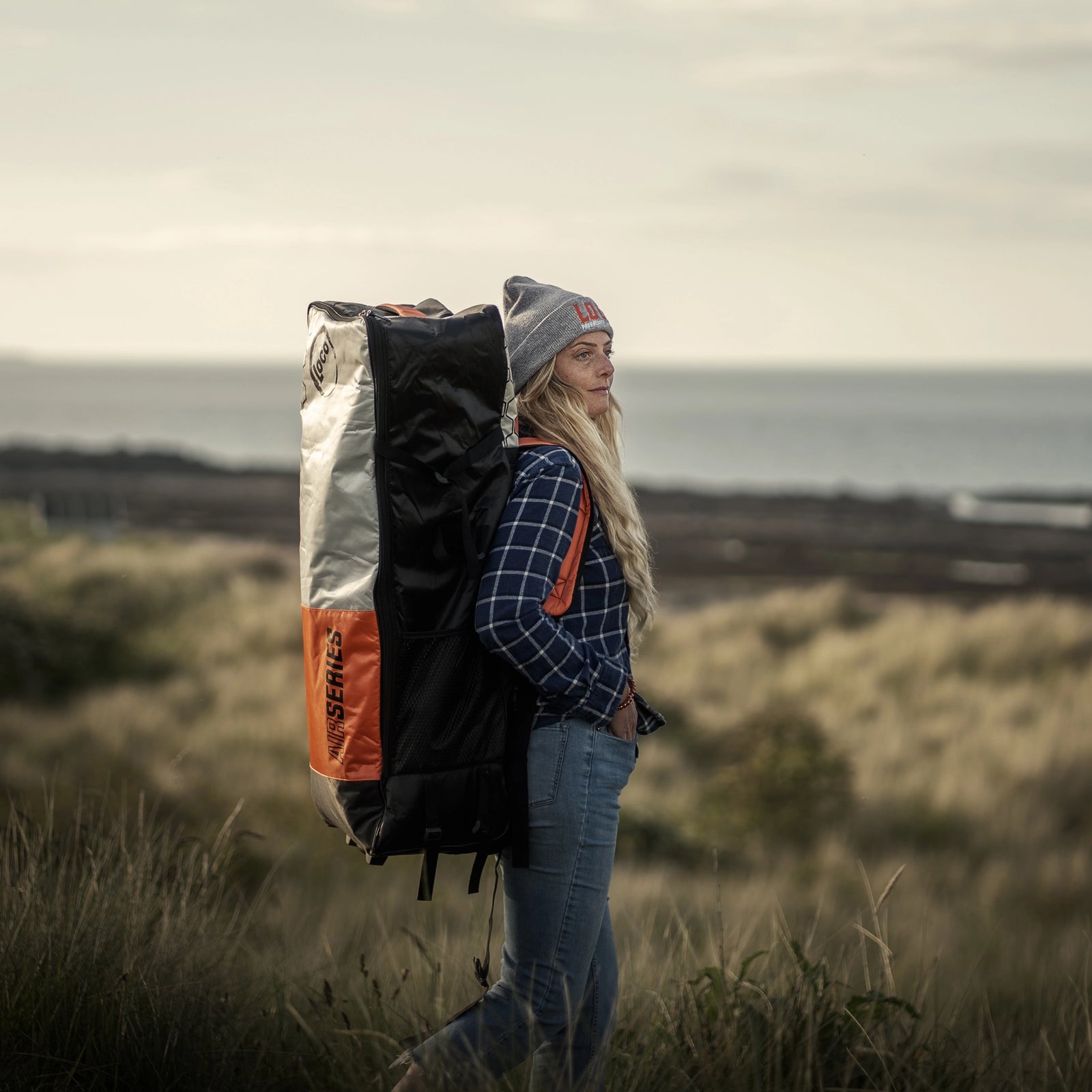 girl hiking with her inflatable paddle board in Northumberland UK