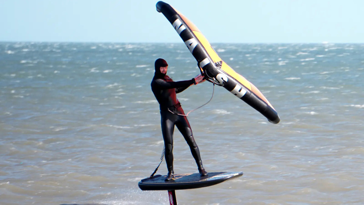 Wingfoiler standing on a stable Loco wingfoil board in bright UK coastal conditions