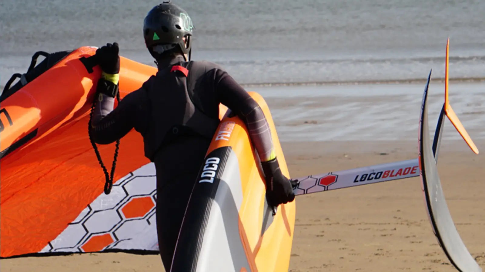 Beginner wing foiler standing on a board with the wing raised on a sheltered UK beach