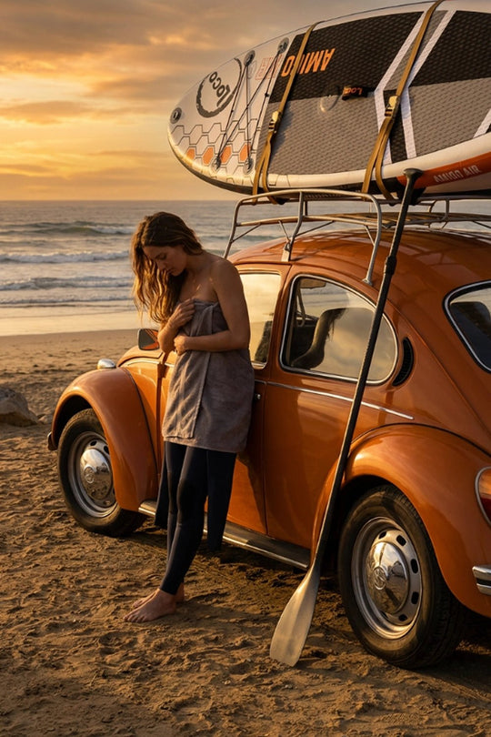 Girl getting changed at beach next to her Beetle with a stand up paddle board on the roof