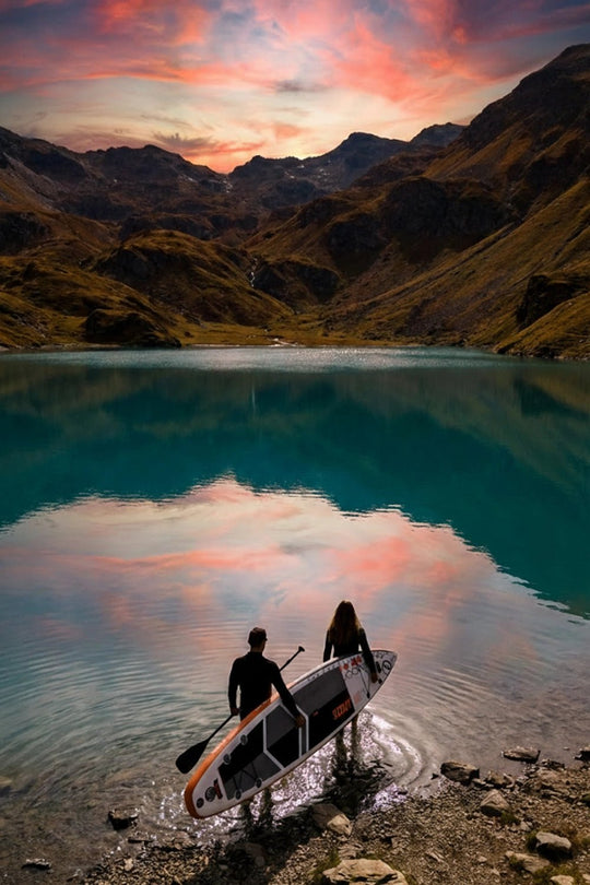 Two people with a paddleboard on a mountain lake at sunset.