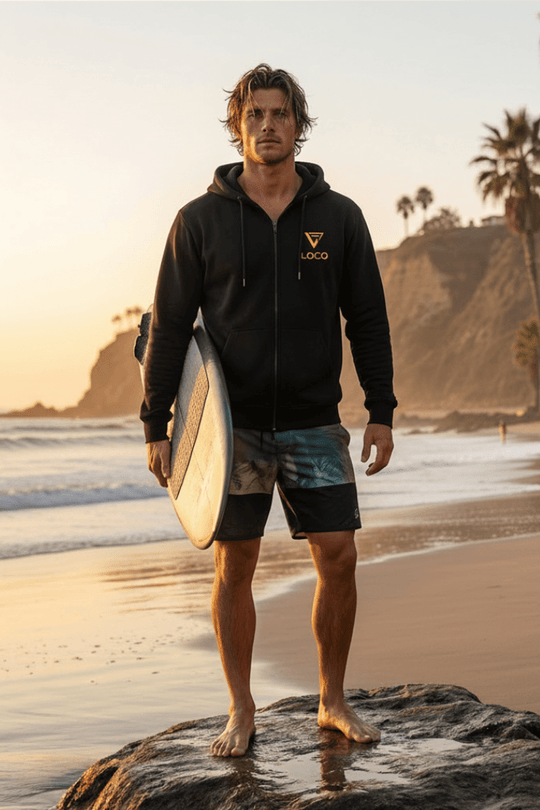 Man holding a surfboard on a beach with palm trees and cliffs in the background
