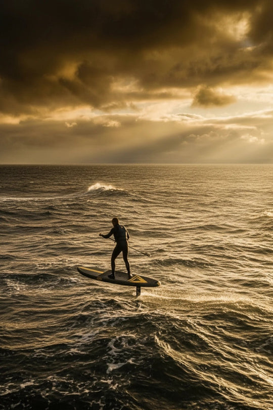 Person downwind SUP foiling on a rough sea with dramatic clouds and sunlight