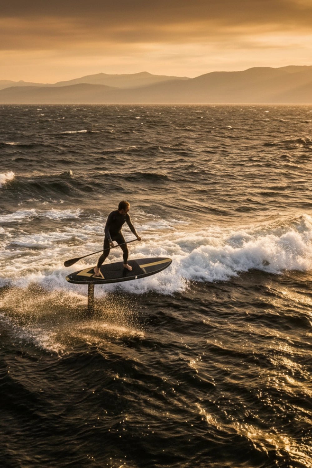 Person paddleboarding on a large body of water with mountains in the background during sunset.