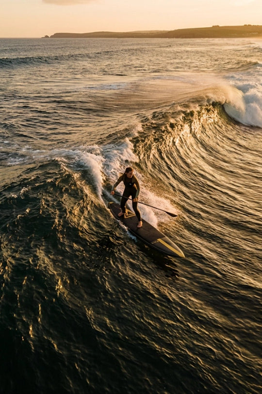 Person paddle surfing on a wave during sunset